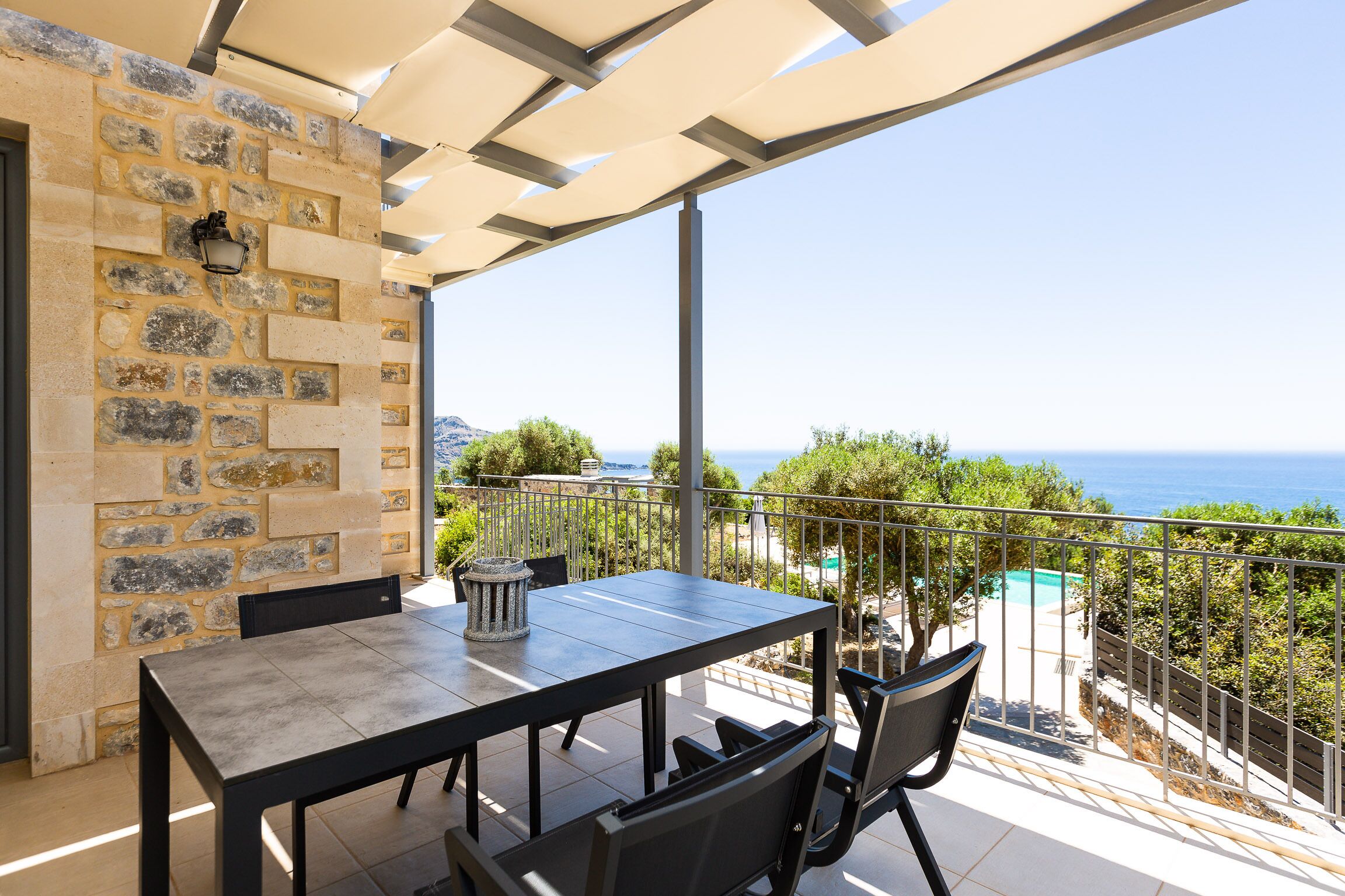 Un balcon avec un mur en pierre, une table avec des chaises et une vue sur la mer.