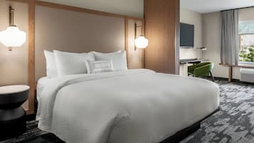 A hotel room with a large bed, a desk, a chair, and a window with curtains.