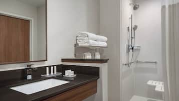 Une salle de bain moderne avec un lavabo au comptoir de couleur sombre, un miroir et un espace douche doté d’une porte en verre.