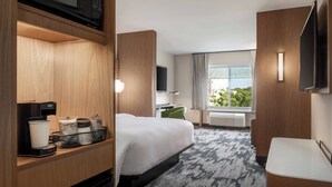 A hotel room with a bed, a desk, a TV, a coffee maker, and a window with a view of greenery. - Fairfield Inn & Suites by Marriott Milwaukee West (Milwaukee)