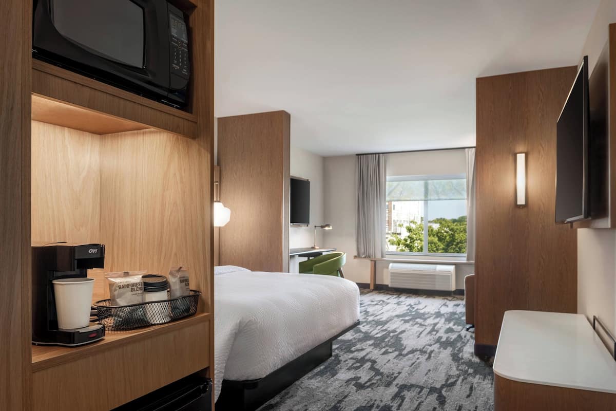A hotel room with a bed, a desk, a TV, a coffee maker, and a window with a view of greenery.