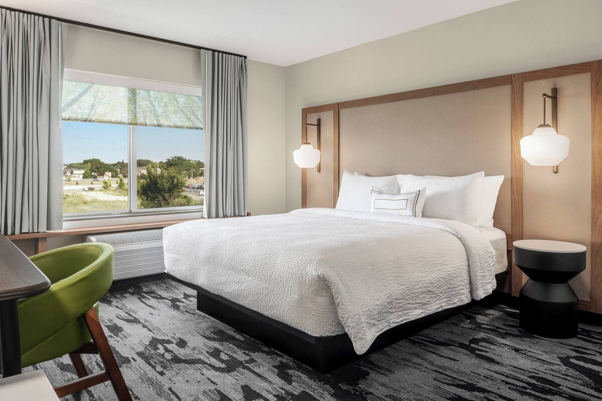 A hotel room with a large bed, a desk, a chair, and a view of the outdoors.