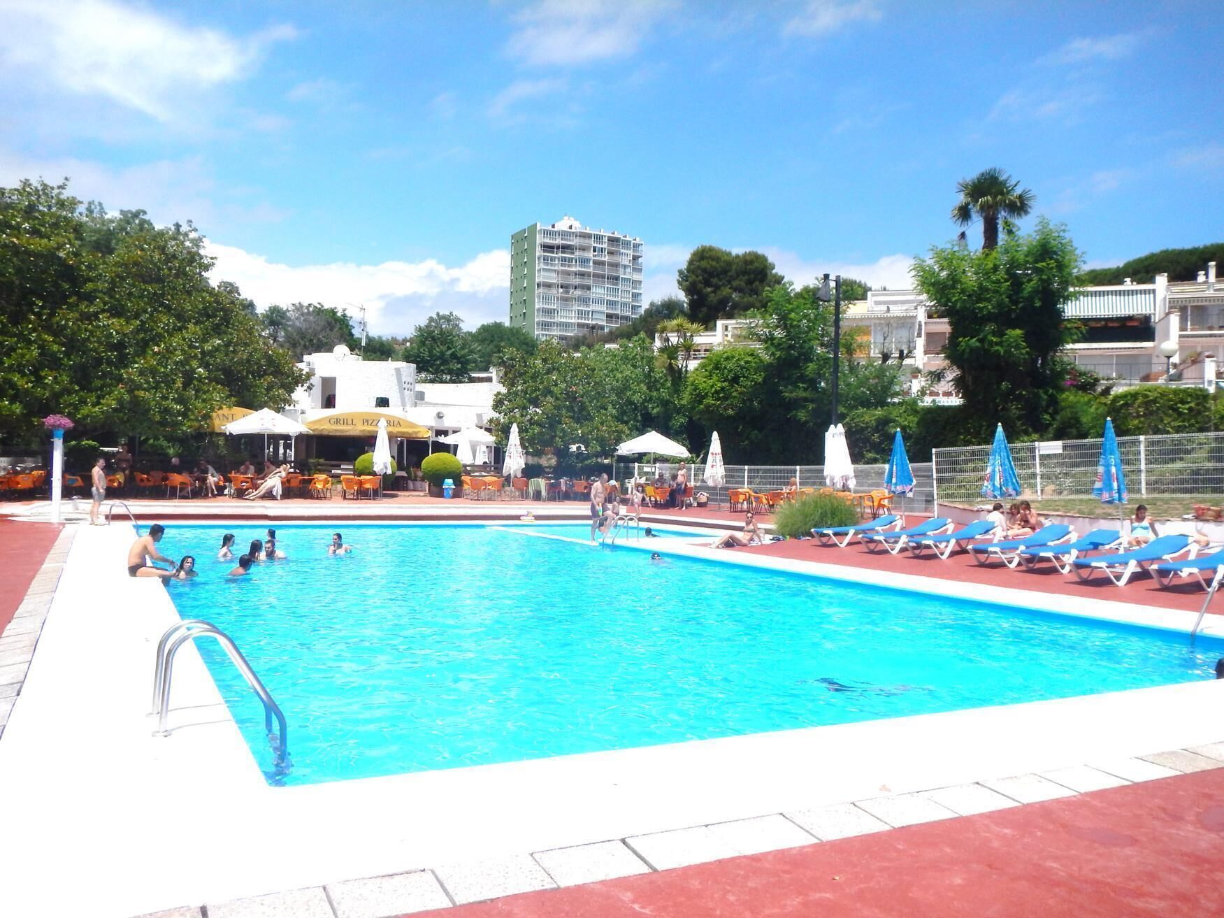 Ein Pool mit Liegestühlen und Sonnenschirmen, umgeben von Grünflächen und Gebäuden.