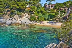 Una platja costanera amb aigua cristal·lina, un litoral rocos i edificis al fons.