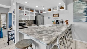A modern kitchen with a marble countertop, built-in appliances, and a bar area with stools. - New Listing! Beachside gem, newly remodeled & redecorated  (South Padre Island)