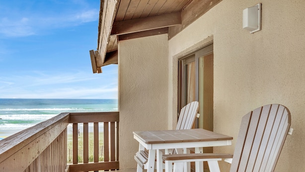A balcony with a wooden railing, a table, and two Adirondack chairs overlooking the ocean. - New Listing! Beachside gem, newly remodeled & redecorated  (South Padre Island)