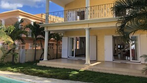 Une maison à plusieurs étages dotée d’un balcon, d’une piscine et de palmiers.