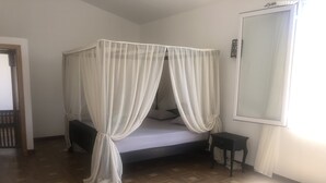 Un lit simple avec un baldaquin, une petite table de chevet et un miroir au mur.