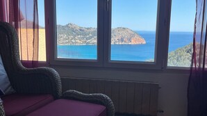 A wicker sofa with a purple cushion in a room with large windows overlooking a coastal landscape.