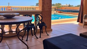 Una terraza con piscina, una mesa y sillas, con vistas a un cielo azul despejado y un paisaje lejano.