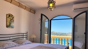 Un dormitorio con cama, lámpara y vistas a un paisaje montañoso a través de puertas abiertas.
