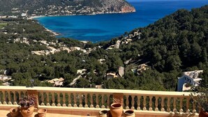 A poolside view overlooking a coastal landscape with a clear blue sky, terraced houses, and a mountainous backdrop.