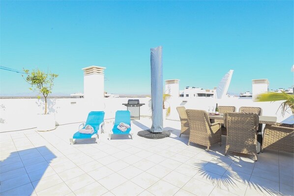 Relax on the outdoor terrace with a clear view of the sky, featuring a wicker dining table and lounge chairs.