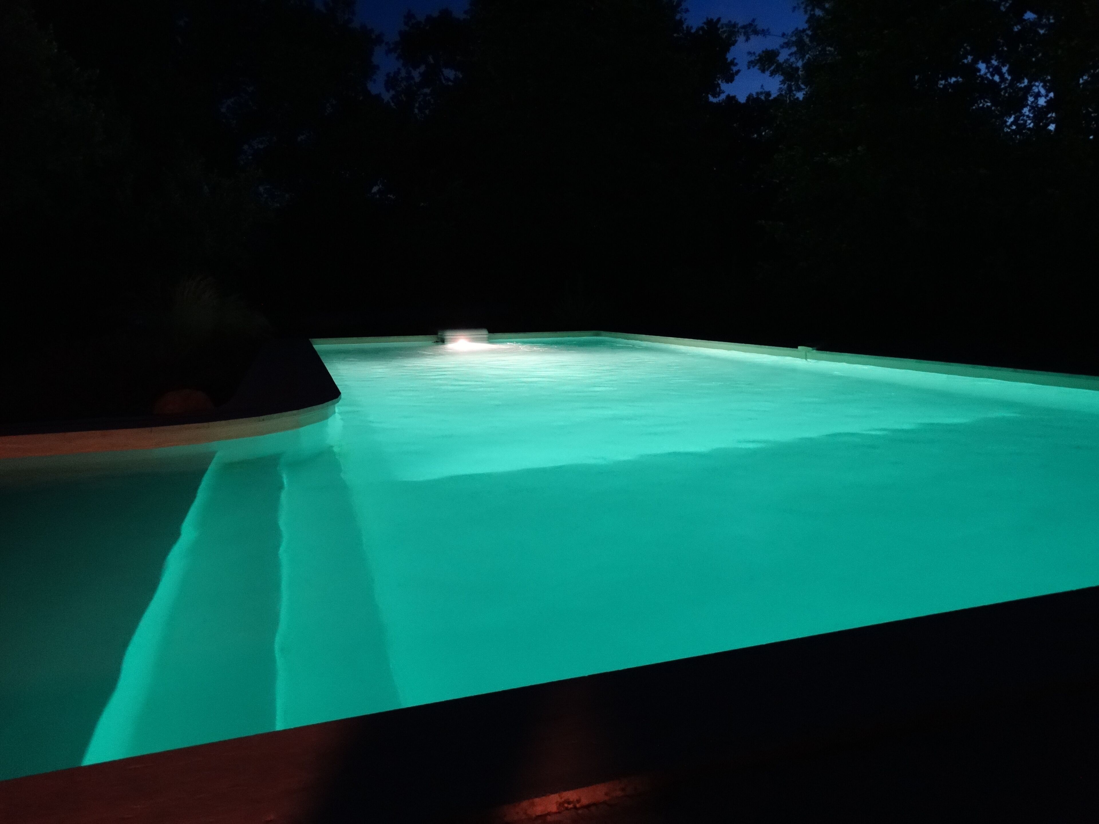 A swimming pool at night with a light source at the far end.