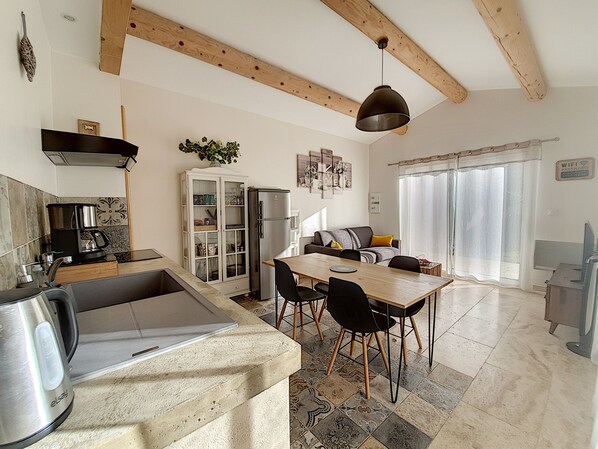 A modern kitchen with a dining area, wooden beams, a refrigerator, and a coffee maker.