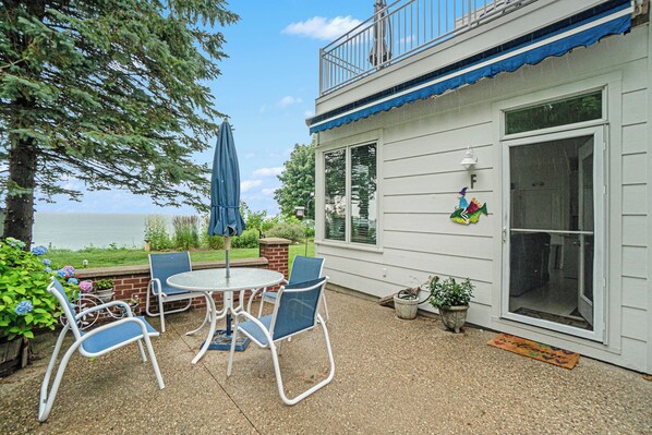 Eine Terrass mit Tisch und Stühlen, einem blauen Sonnenschirm und Blick auf das Wasser.