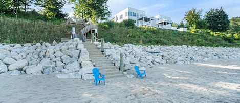 A beach with two blue chairs, a stone wall, and a staircase leading to a building.