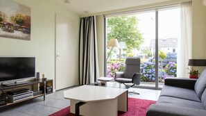Relax in this stylish living room with a flat-screen TV, comfortable sofa, and armchair, offering a serene view of the garden.