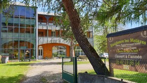 A modern building with a glass facade and wooden accents, a signboard advertising a hotel with 2-4 bedrooms starting from 59€ per night, and a date of opening. - Résidence Les Mélèzes de Prades (Prades)