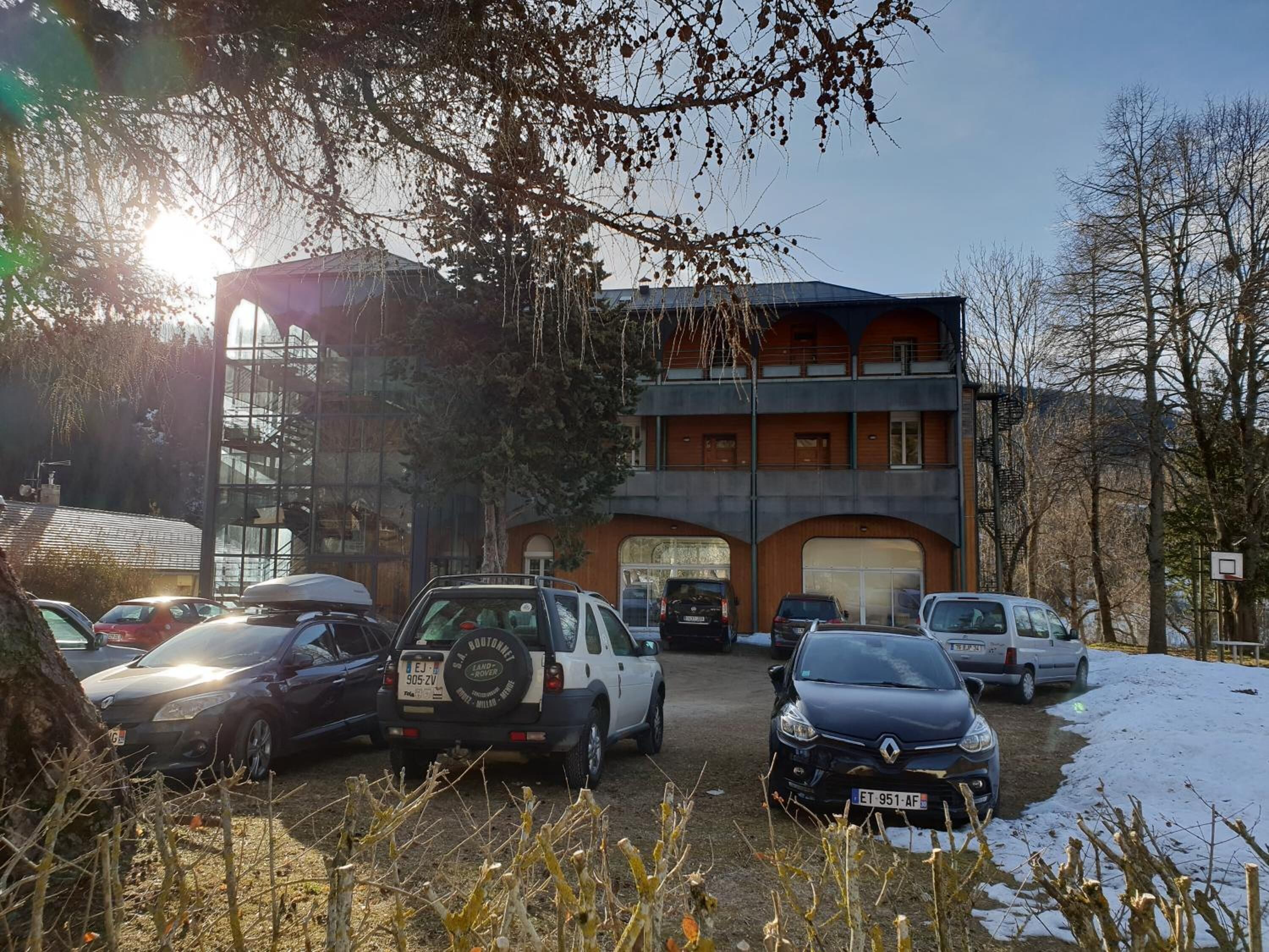 A multi-story building with a garage, parked cars, and a basketball court.