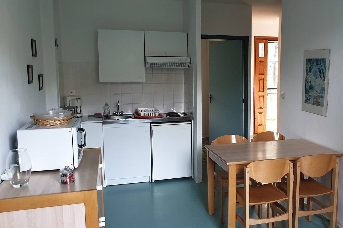 A compact kitchen with white cabinets, a small refrigerator, and a dining area with a wooden table and chairs.