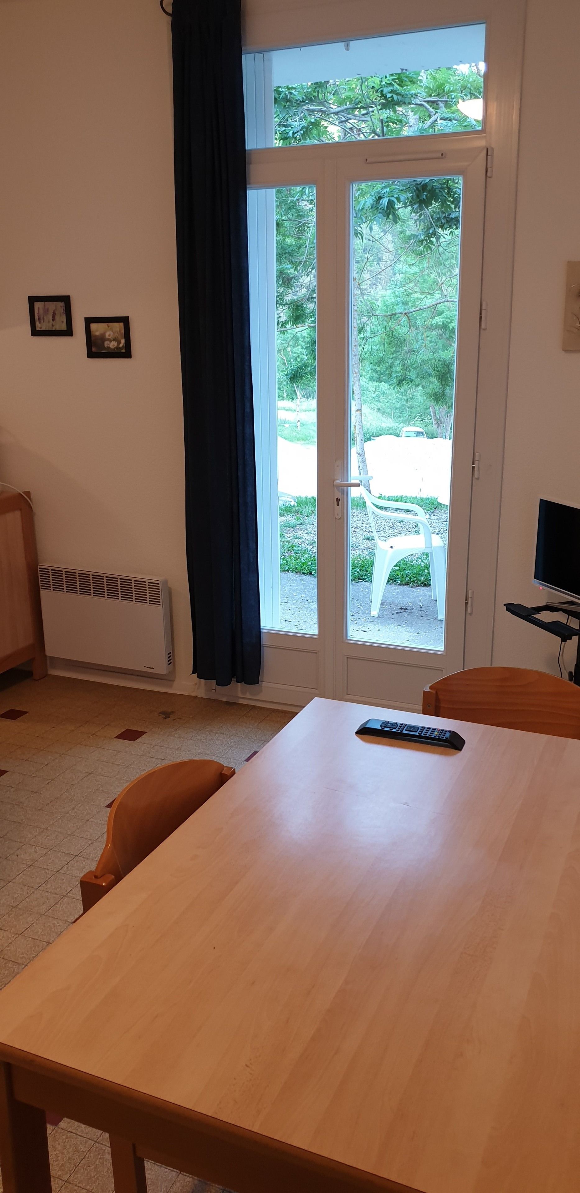 Une pièce comprenant une table en bois, une chaise, un radiateur, un téléviseur et une porte donnant sur un jardin.
