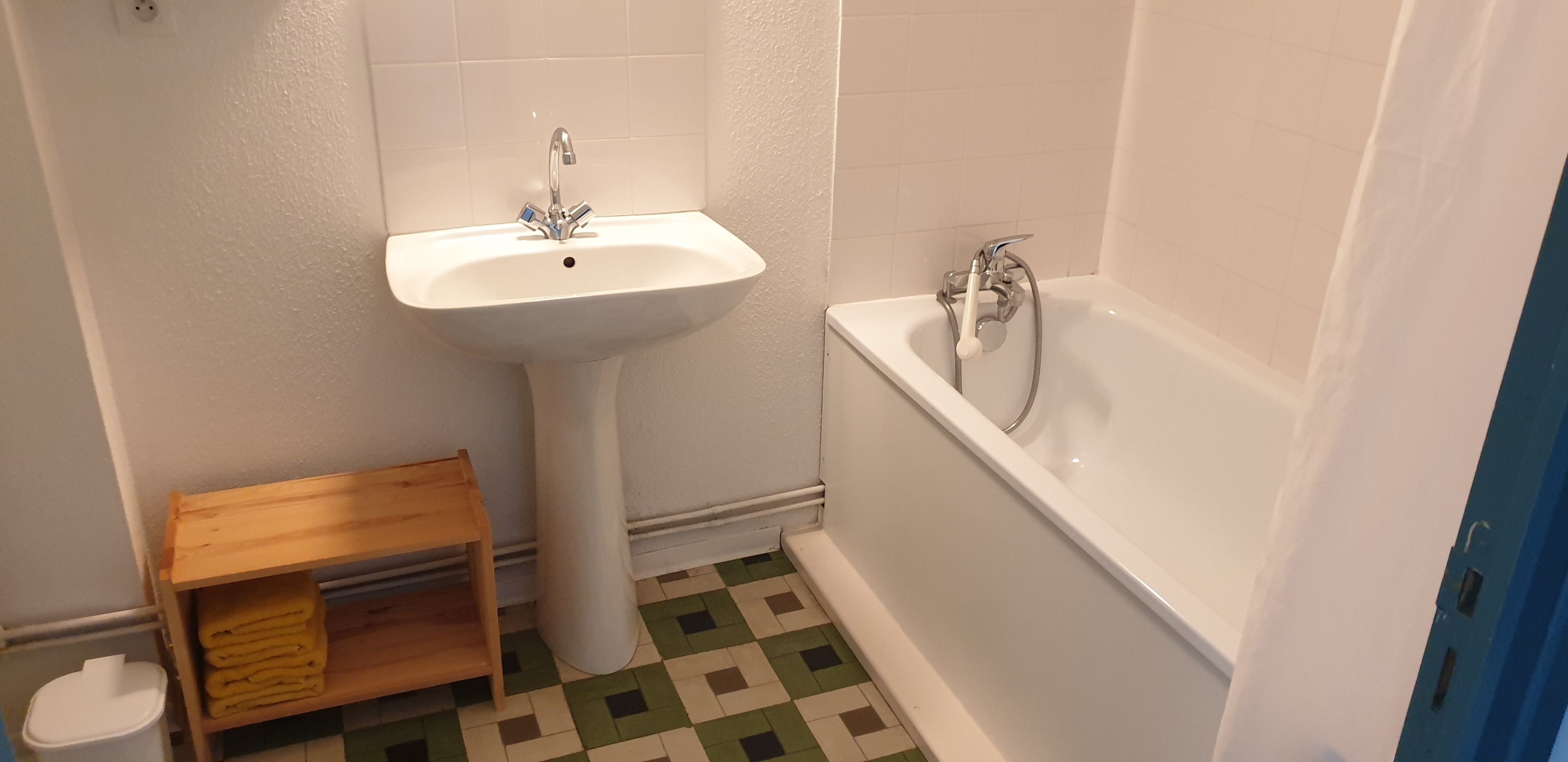 Une salle de bain avec un lavabo sur colonne, une baignoire et une petite étagère en bois.
