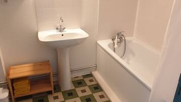 Une salle de bain avec un lavabo sur colonne, une baignoire et une petite étagère en bois.