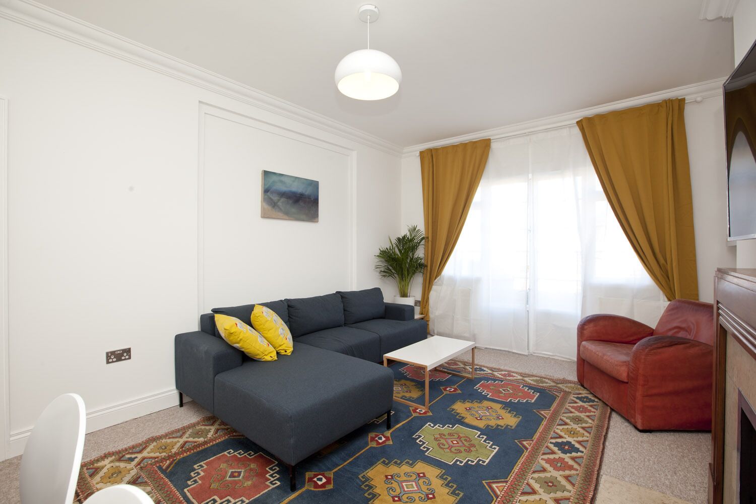 A modern living room with a grey sofa, a small white table, a red armchair, and a patterned rug.