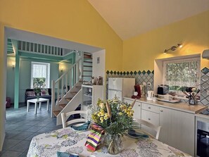 A dining area with a table set for two, a kitchen with a refrigerator and stove, and a staircase leading to an upper level.
