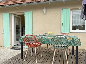 Un espace extérieur aménagé pour prendre les repas, avec une table et des chaises, un saladier rempli de fruits et une porte donnant accès à un bâtiment.