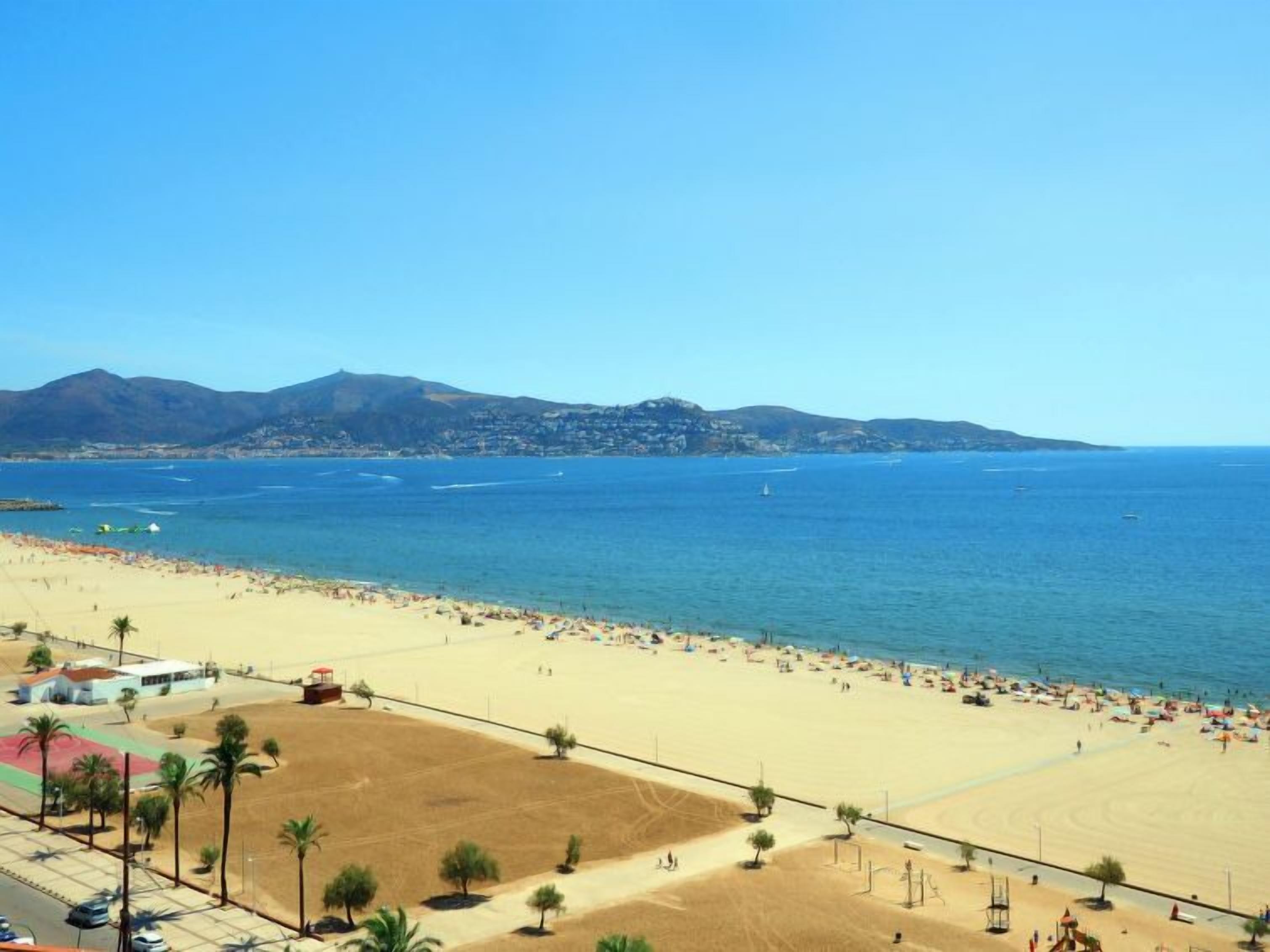 Een strand met een helder uitzicht op de zee en bergen op de achtergrond.
