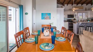 Uma sala de jantar com uma mesa de madeira posta para seis pessoas, rodeada por cadeiras. Um quadro está pendurado na parede acima da mesa.