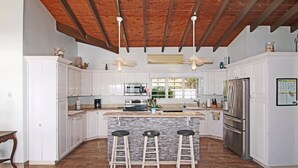 Uma cozinha com armários brancos, uma ilha central com banquetas, forno embutido e geladeira.