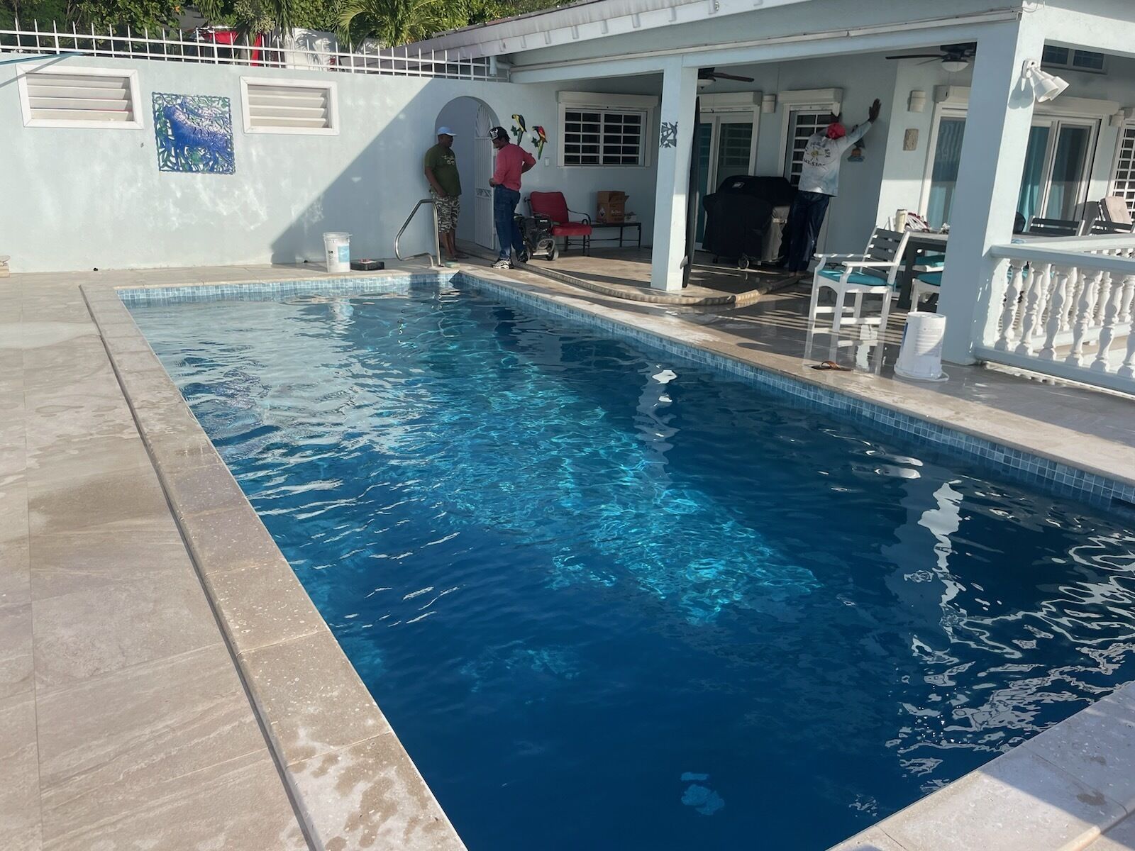 A swimming pool with clear blue water, surrounded by a white fence and a covered patio area.
