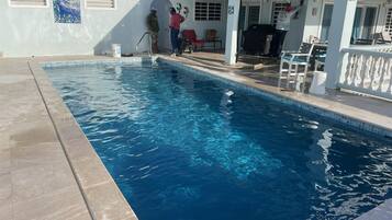 A swimming pool with clear blue water, surrounded by a white fence and a covered patio area.