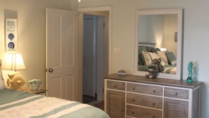 Quarto com cama, cômoda, espelho e porta que dá para um corredor.