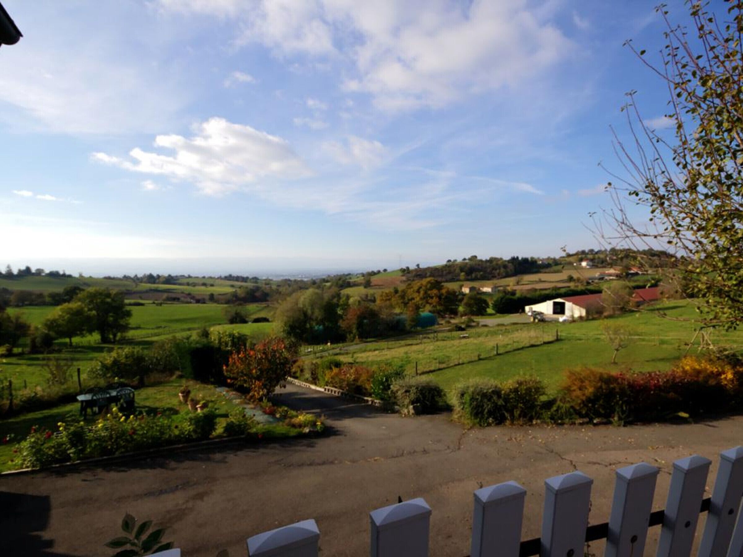 A rural landscape with rolling green fields, a white building with a red roof, and a clear blue sky.
