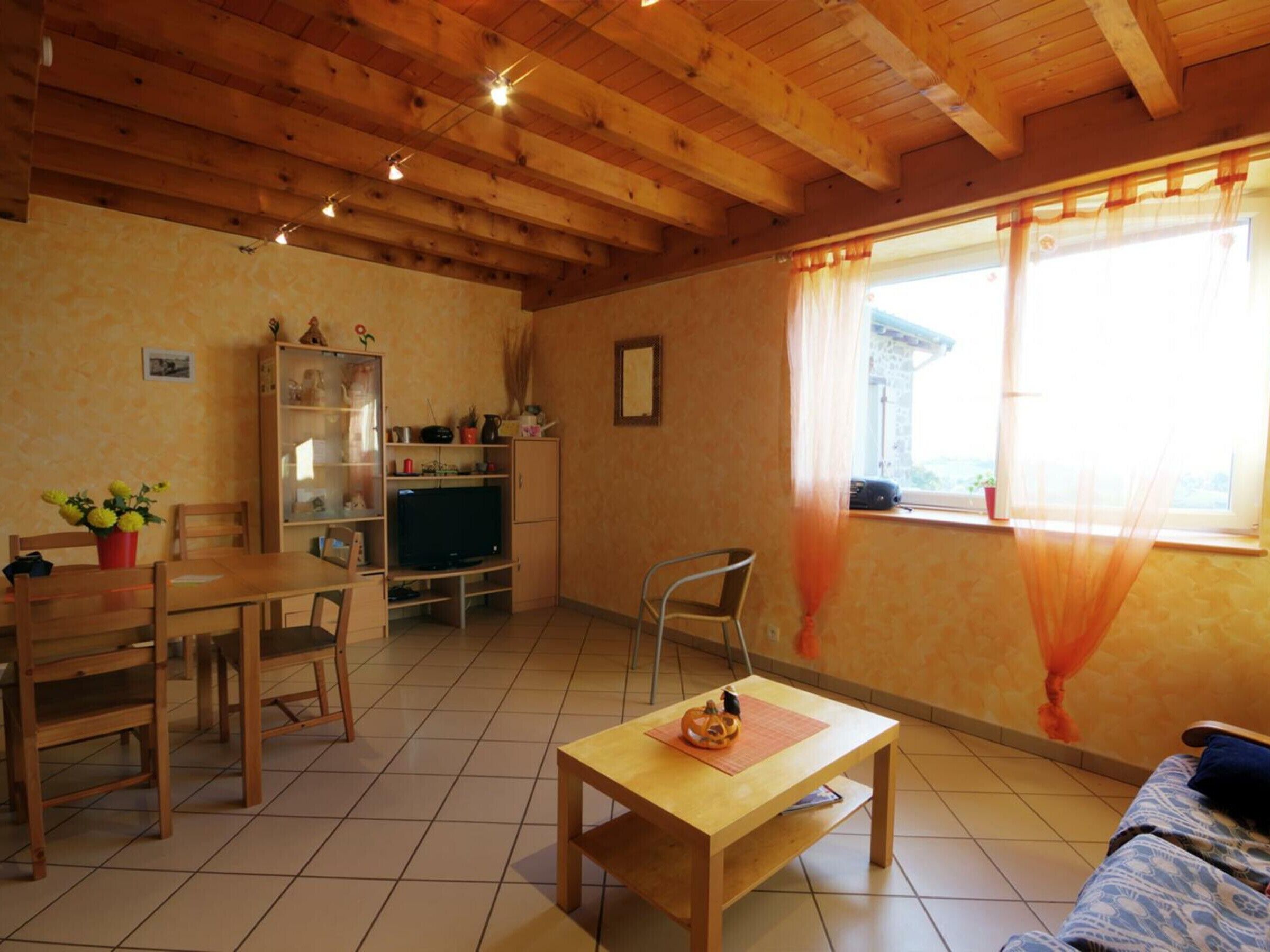 A cozy room with a wooden ceiling, a dining table with chairs, a TV, and a window with curtains.