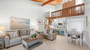 A spacious living area with two sofas, a coffee table, and a dining table with chairs. A staircase leads to an upper level with a kitchen and dining area.