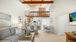 A spacious living area with a high ceiling, a staircase to an upper level, a dining area, and a kitchen.