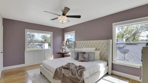 Une chambre avec un grand lit, un ventilateur de plafond, une fenêtre et une vue sur l’extérieur.
