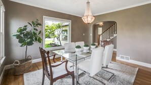 Un espace repas avec une table en verre, des chaises blanches, un lustre et une vue sur l’extérieur.