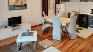 Una sala de estar moderna con un televisor de pantalla plana, una mesa de comedor con sillas, una pequeña mesita auxiliar y un cuadro de un velero en la pared.