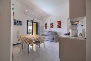 A modern kitchen with white cabinets, a dining table with a floral tablecloth, and a gray sofa. - La Palma - Apartment with terrace and pool view (Lazise)