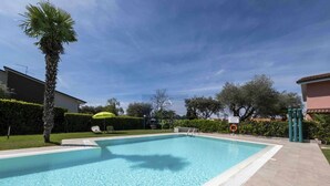 A rectangular swimming pool with clear blue water, surrounded by a paved deck. There are lounge chairs and a green umbrella near the pool. - La Palma - Apartment with terrace and pool view (Lazise)