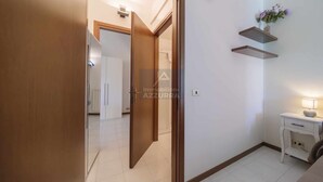 A hallway with a wooden door, a white wall with a shelf, and a small table with a lamp. - La Palma - Apartment with terrace and pool view (Lazise)