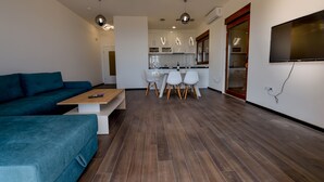 A modern living room with a teal sofa, a wooden coffee table, and a dining area with white chairs and a kitchen in the background. - Dubrovnik Heights Luxury Villa (Ravno)