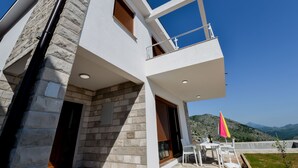 A modern building with a stone facade, a balcony with a railing, and a table with chairs outside. - Dubrovnik Heights Luxury Villa (Ravno)