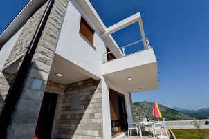 A modern building with a stone facade, a balcony with a railing, and a table with chairs outside.